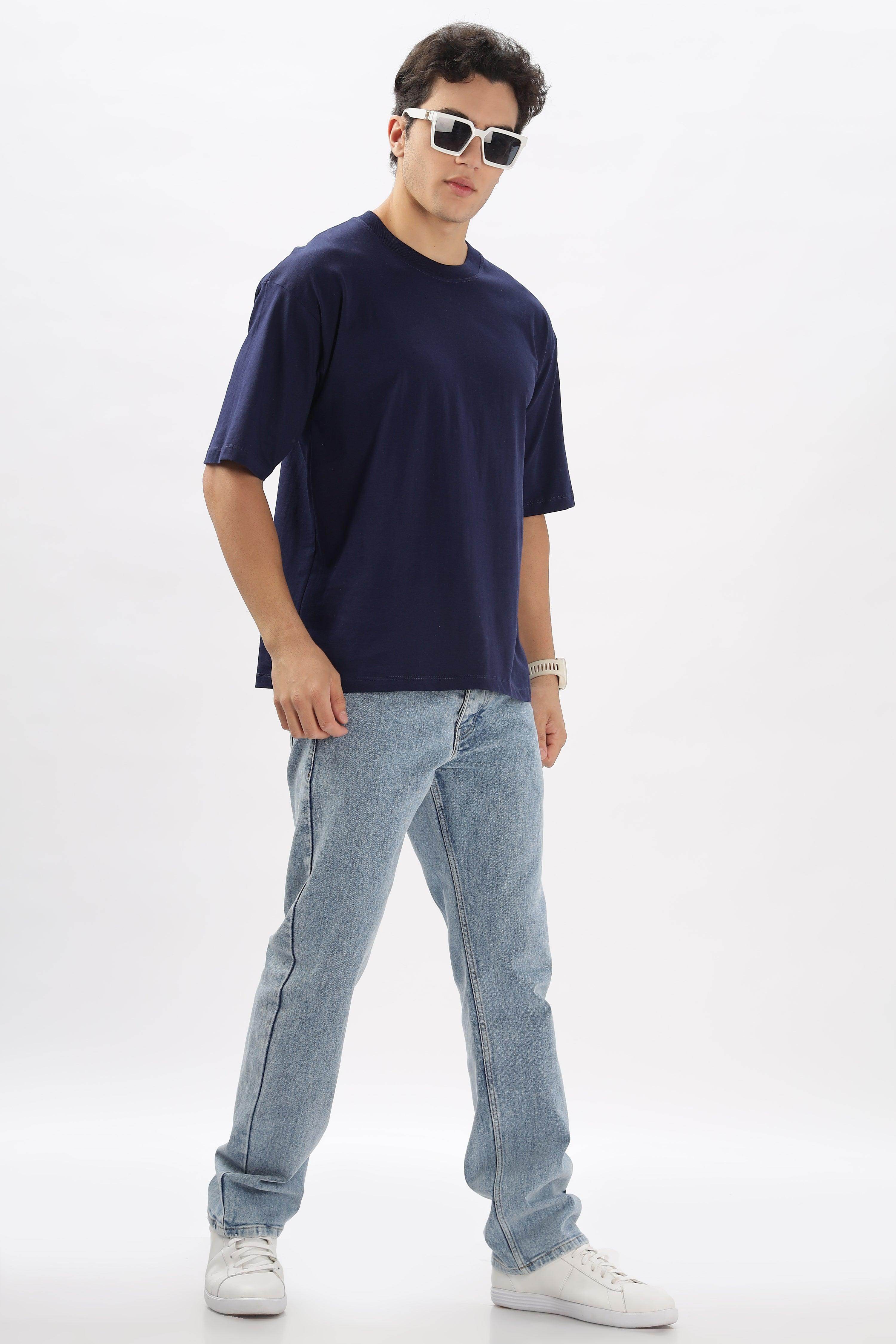Male model wearing navy oversized solid t shirts for men paired with light blue jeans and white sneakers