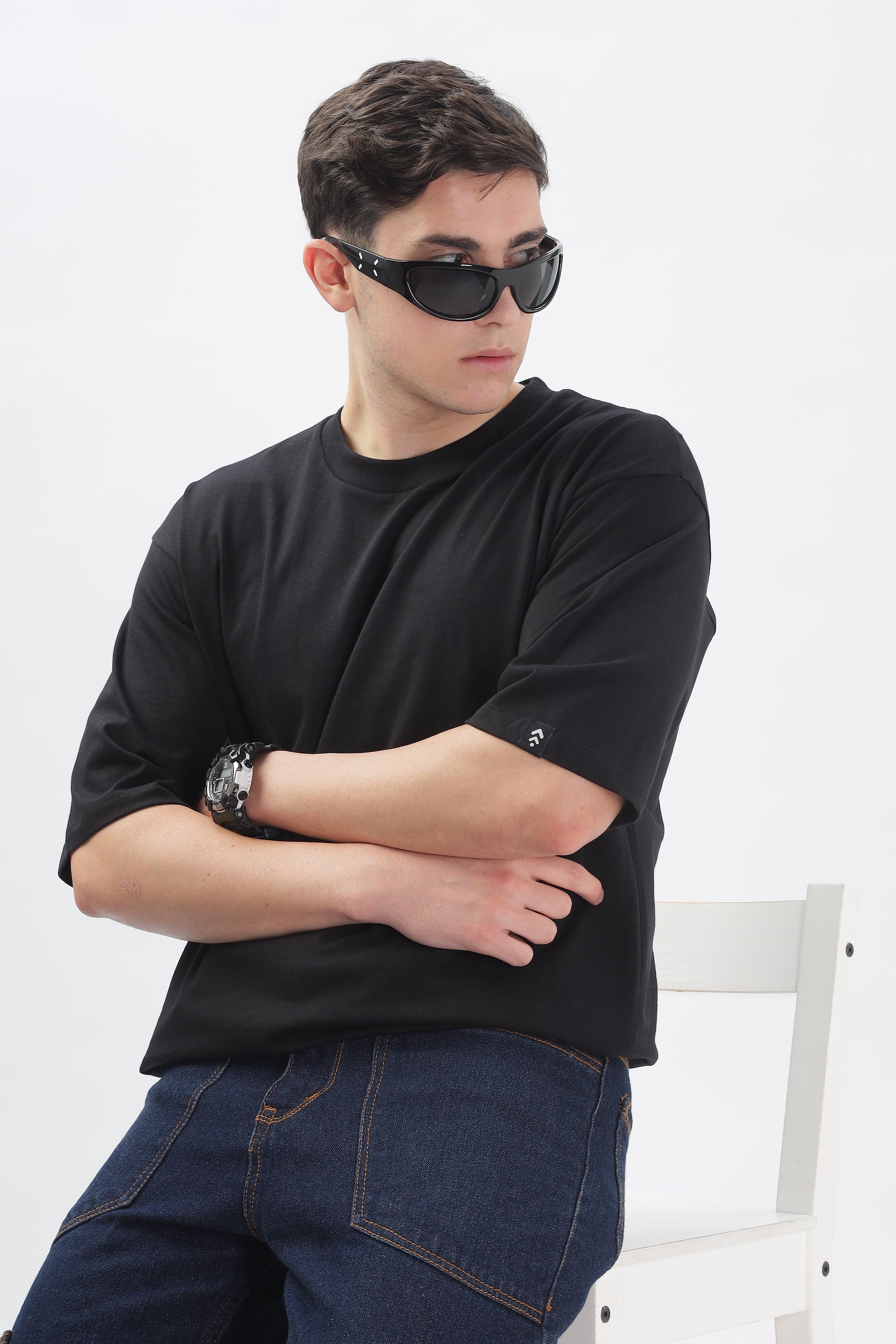 Soulmonk black oversized t-shirt for men worn by model with sunglasses and jeans sitting on white chair