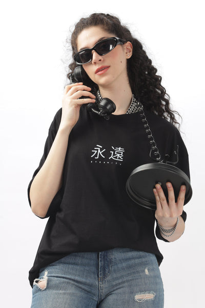 Woman wearing black oversized t-shirt for women with white text and distressed jeans holding a retro phone
