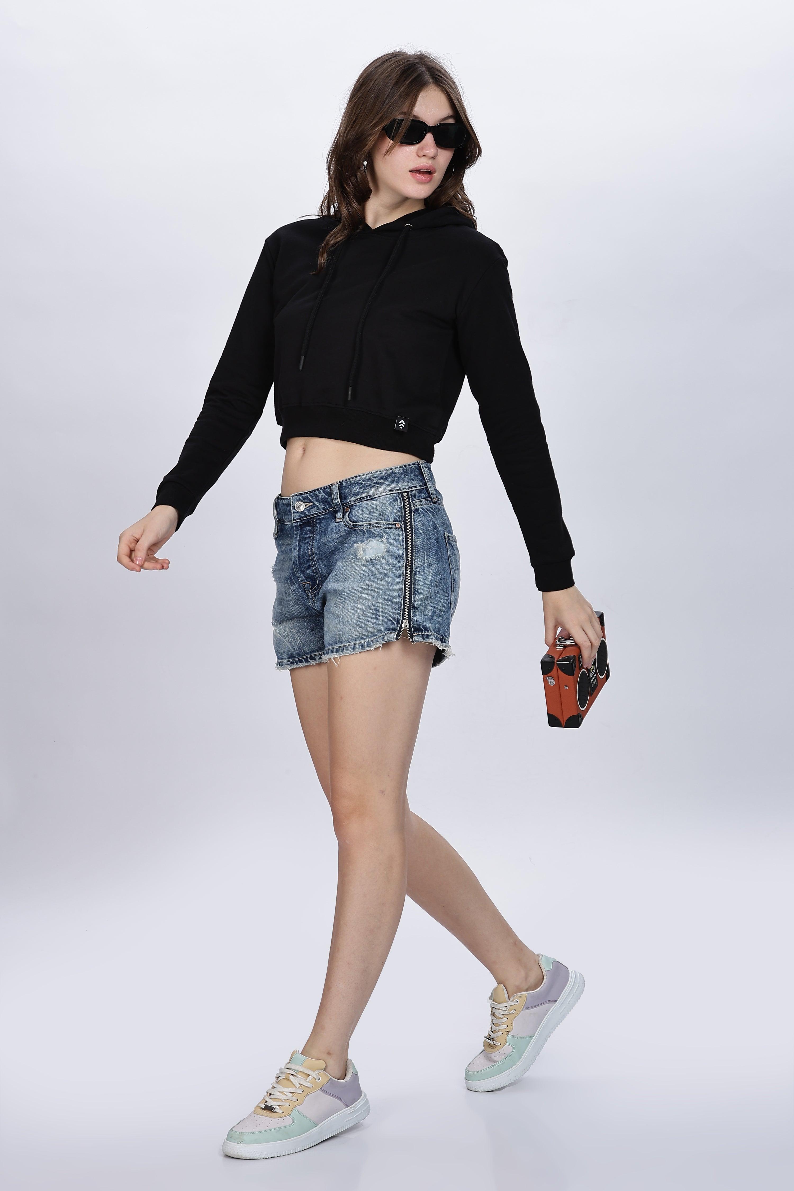 Woman wearing a black crop hoodie for women paired with denim shorts and sneakers