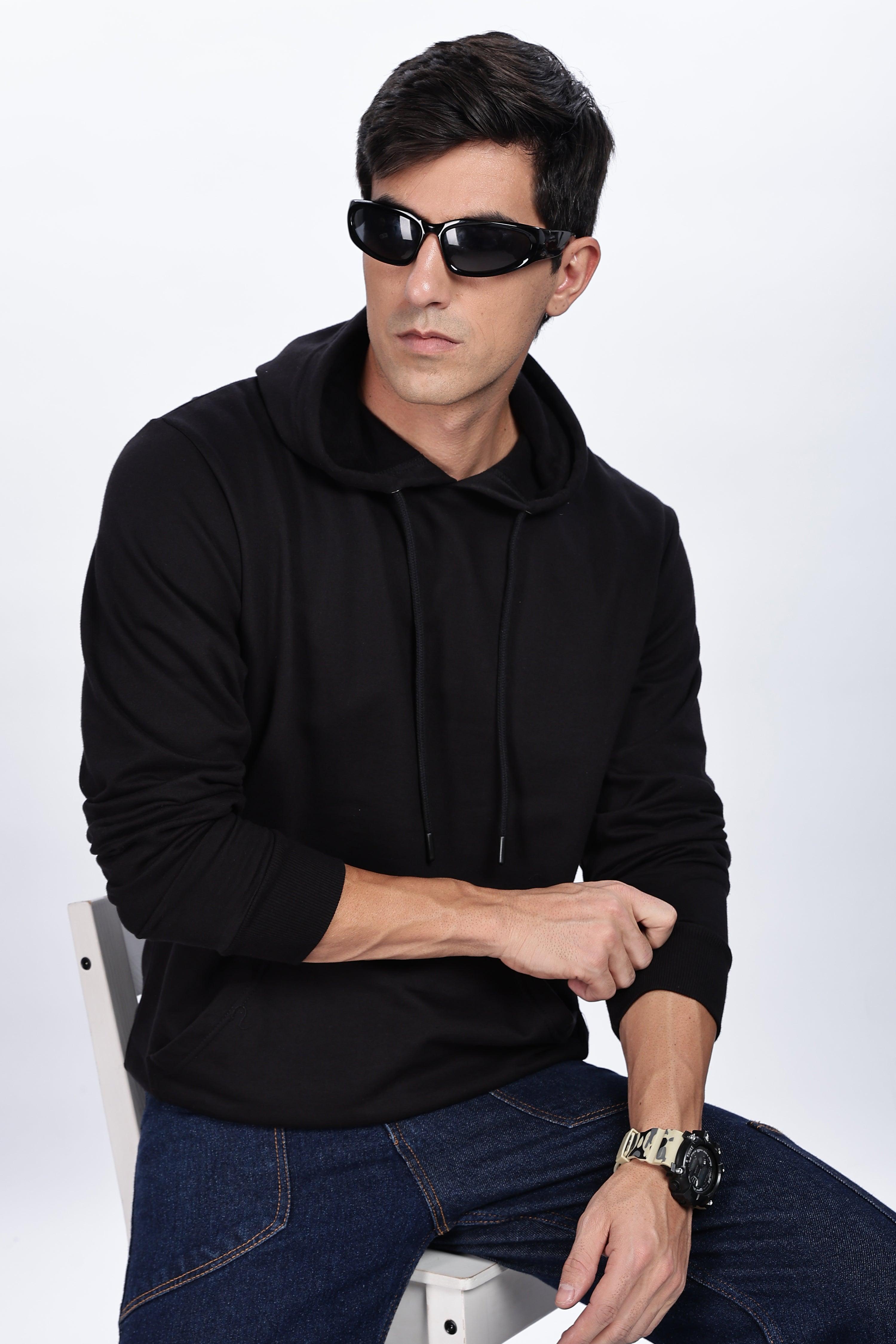 Male model wearing Soulmonk midnight black hoodie with sunglasses and watch seated on white chair