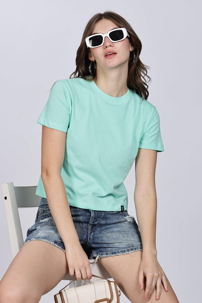 Woman wearing a mint green crop top for women paired with denim shorts and white sunglasses