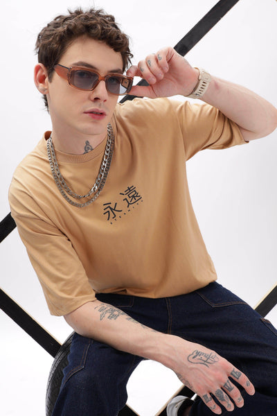 Male model wearing a taupe oversized t-shirt with black graphic text paired with dark jeans and sunglasses